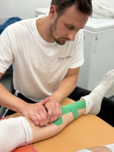 Sportphysiotherapeut behandelt Bein eines Athleten mit Tape in Leipzig